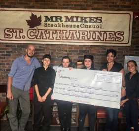 A group of people at Mr MIKES Steakhouse St. Catharines hold a large check for $2,800, presented to Autism Ontario.