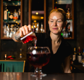 A bartender pours a red cocktail into a large glass at Mr MIKES Steakhouse.
