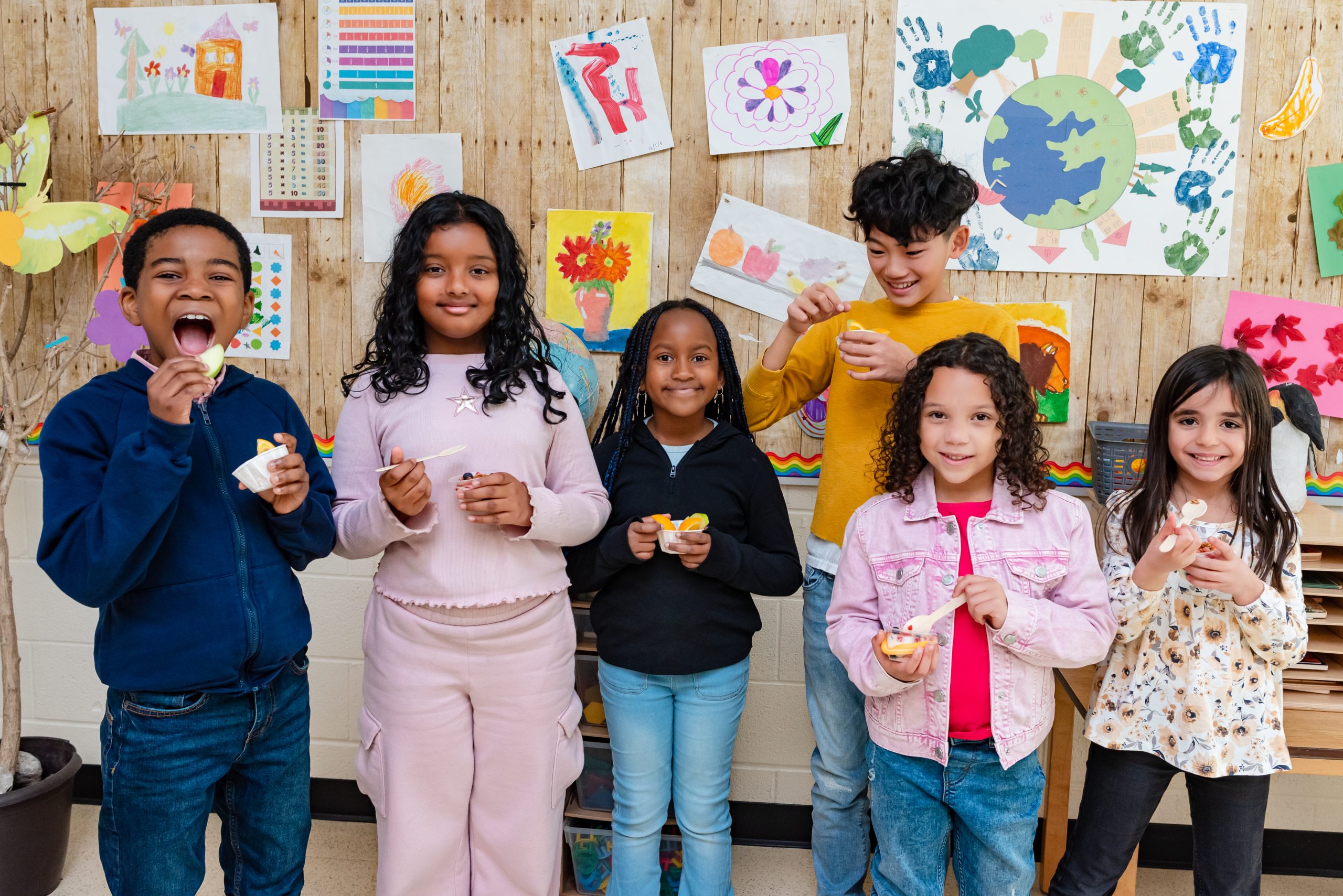 Children smiling and holding snacks as part of the Make Happy Tummies community initiative, with colorful artwork in the background