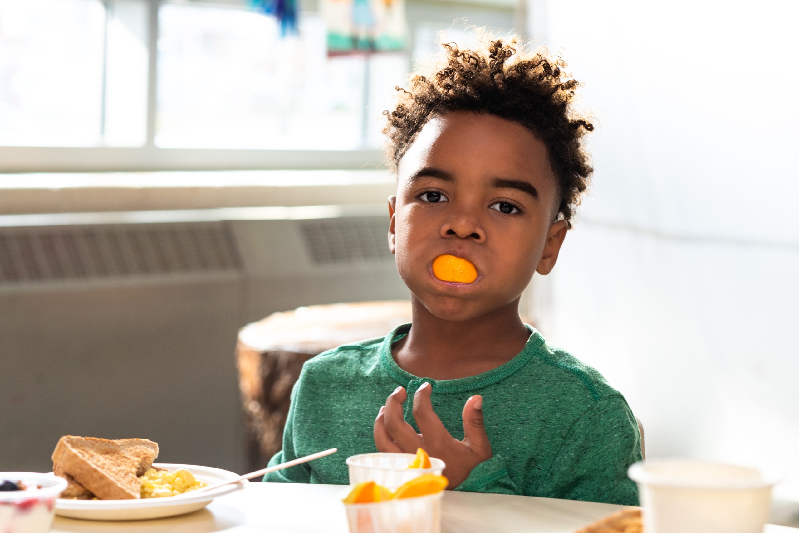 A kid enjoying a snack as part of the Make Happy Tummies initiative, seated at a table with snacks and drinks.